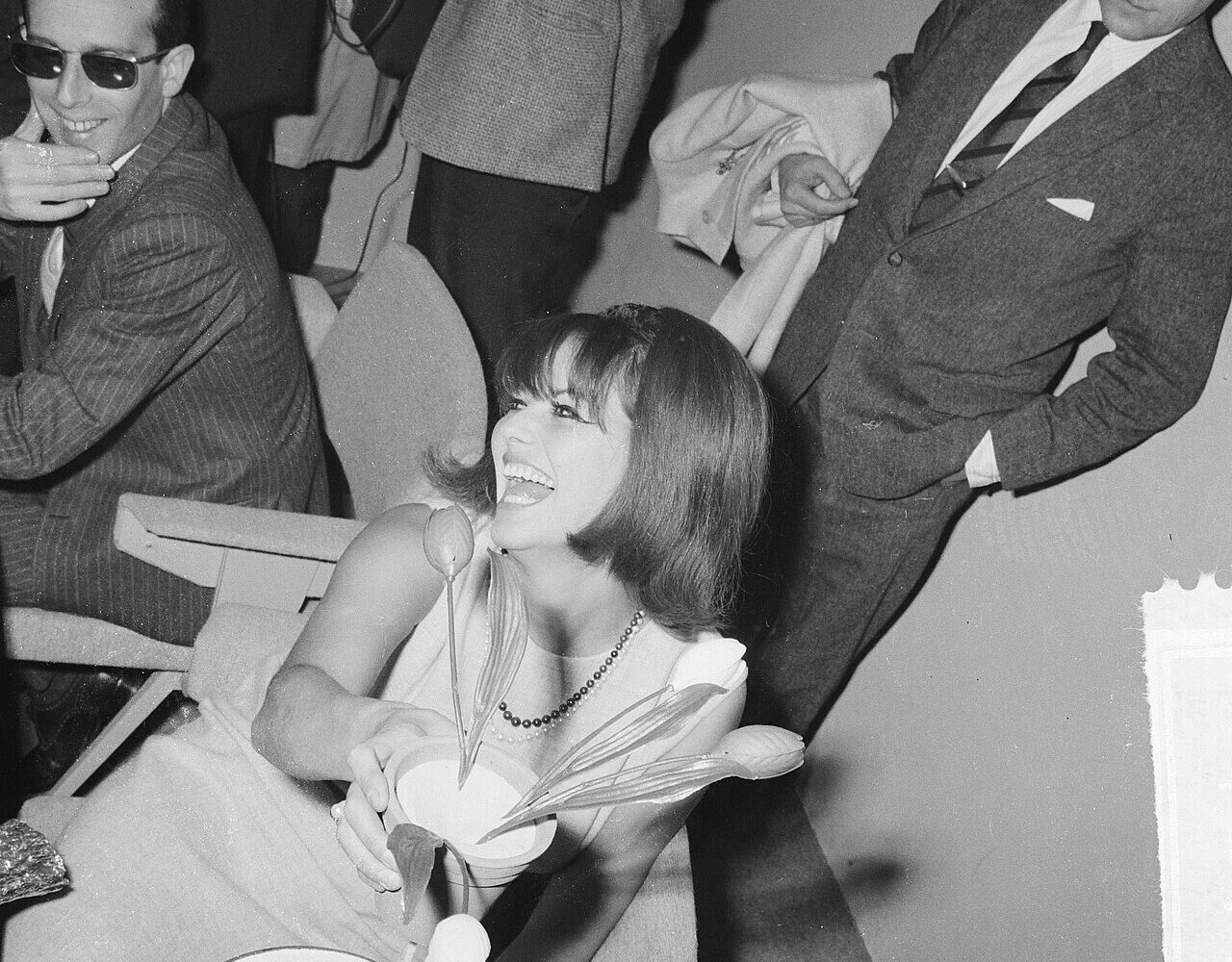 Claudia Cardinale souriante, un bouquet à la main, à l'aéroport de Schiphol le 16 décembre 1964