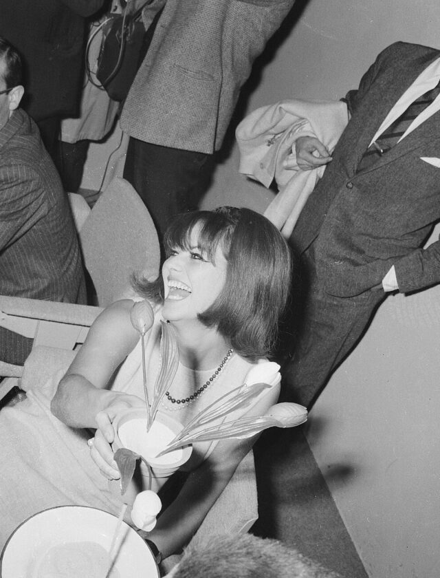 Claudia Cardinale souriante, un bouquet à la main, à l'aéroport de Schiphol le 16 décembre 1964
