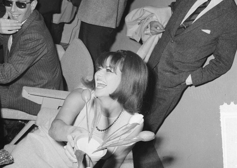 Claudia Cardinale souriante, un bouquet à la main, à l'aéroport de Schiphol le 16 décembre 1964