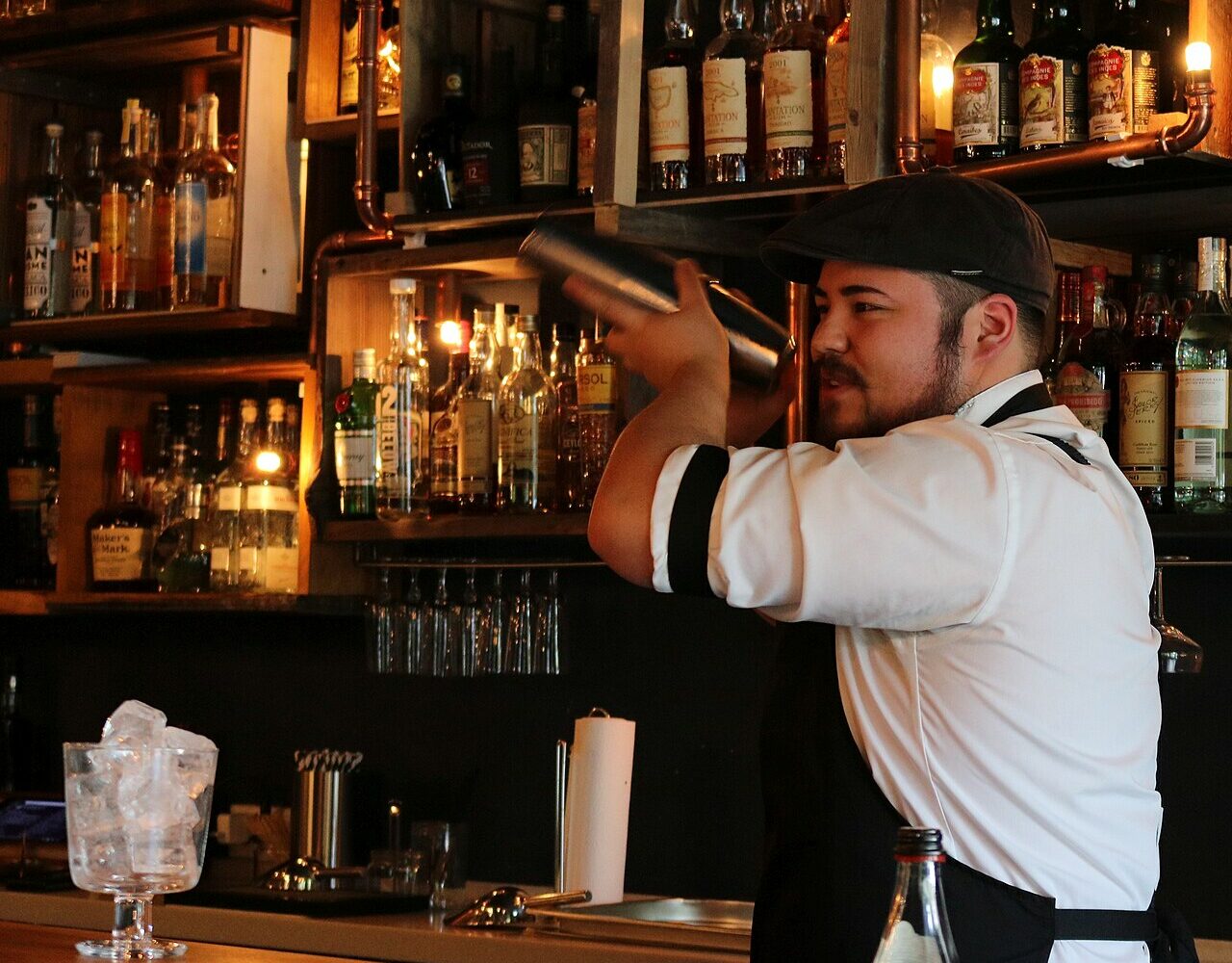Un barman secoue un shaker devant un mur de bouteilles
