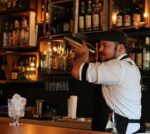 Un barman secoue un shaker devant un mur de bouteilles
