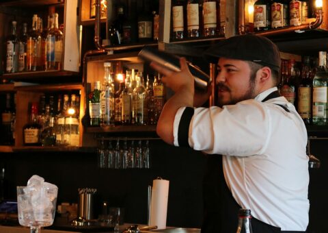 Un barman secoue un shaker devant un mur de bouteilles