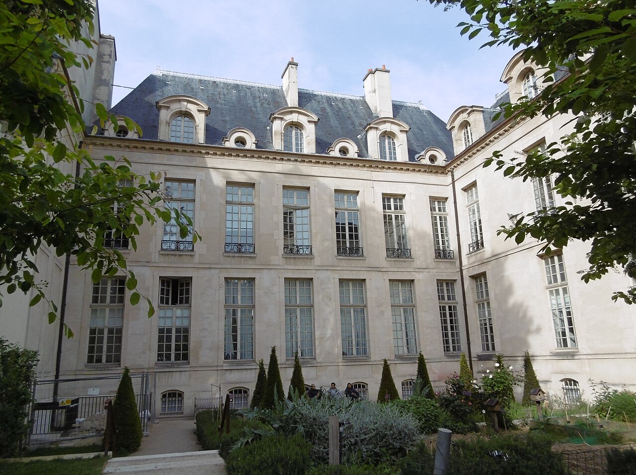 La façade classique de l'hôtel d'Albret vue depuis le jardin des Rosiers, ses ifs taillés et ses massifs