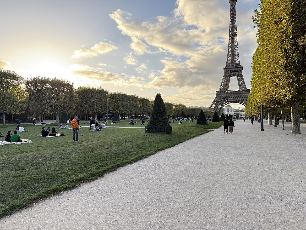 La grande pelouse du Champ-de-Mars, son allée de gravier bordée d'arbres taillés et la tour Eiffel dans l'axe