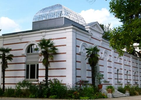 Le pavillon de l'Indochine du jardin d'agronomie tropicale, façade blanche à bandes rouges et coupole de verre, entouré de palmiers