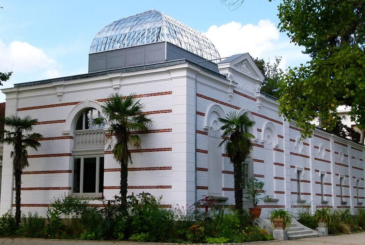 Le pavillon de l'Indochine du jardin d'agronomie tropicale, façade blanche à bandes rouges et coupole de verre, entouré de palmiers
