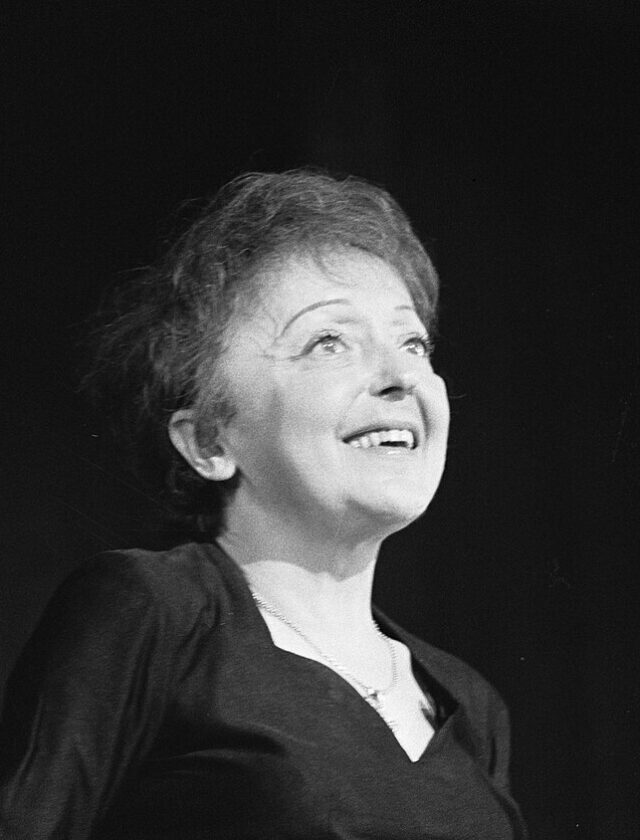 Édith Piaf chantant, le visage levé, devant un micro à Rotterdam le 13 décembre 1962