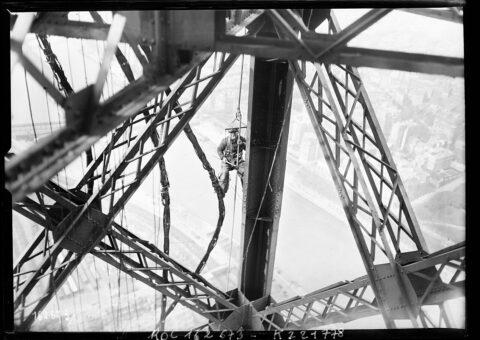 Un peintre suspendu dans la charpente de la tour Eiffel au-dessus de la Seine, photographie de presse