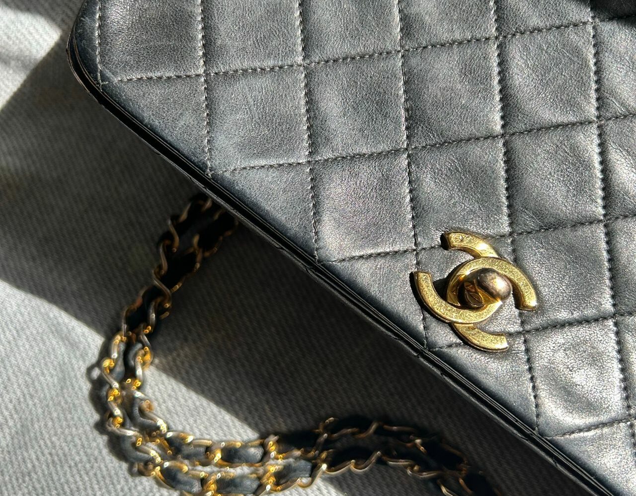 Gros plan d'un sac Chanel en cuir noir matelassé avec sa chaîne dorée entrelacée de cuir